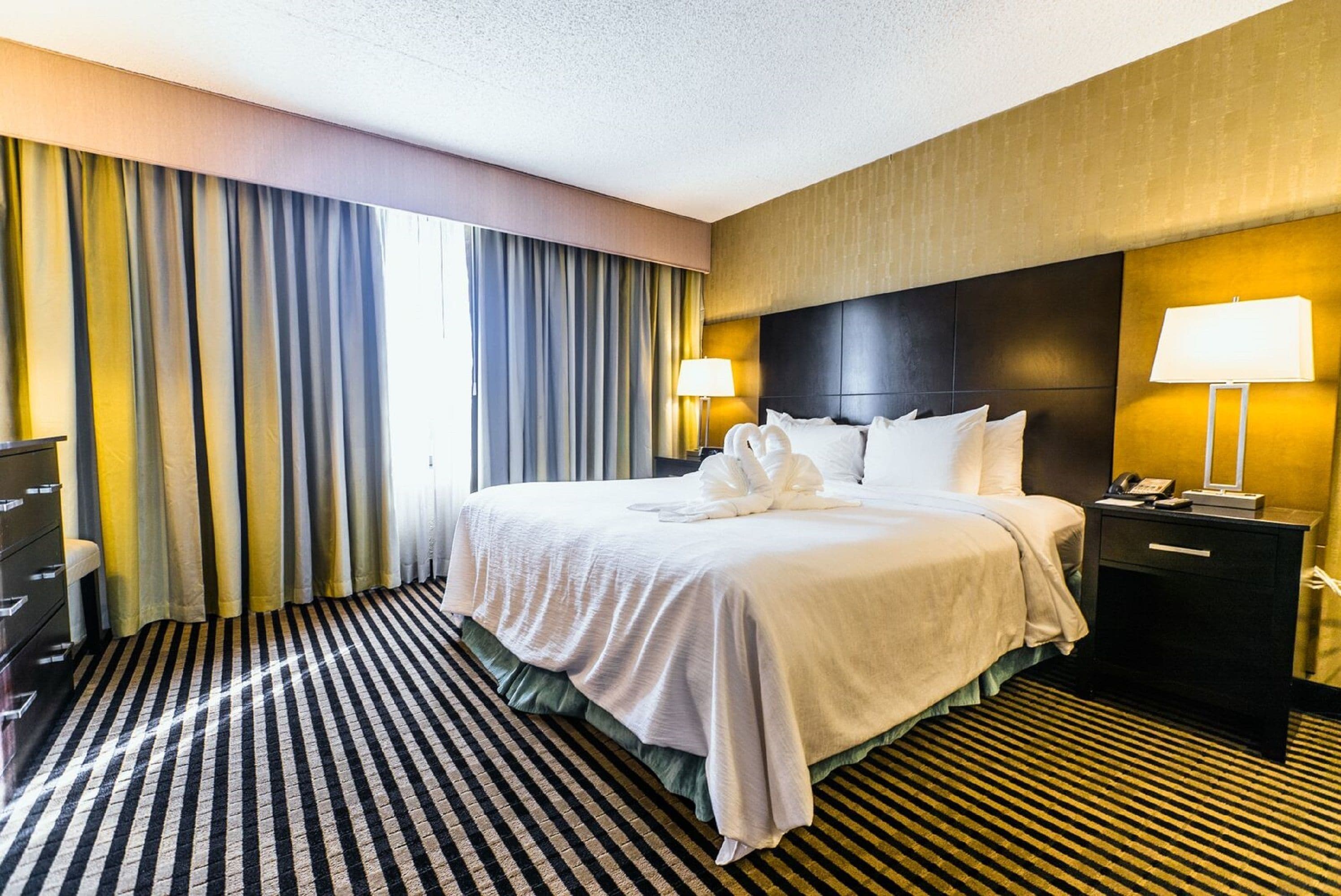 A hotel room with a large bed, two bedside lamps, a dresser, and a striped carpet.