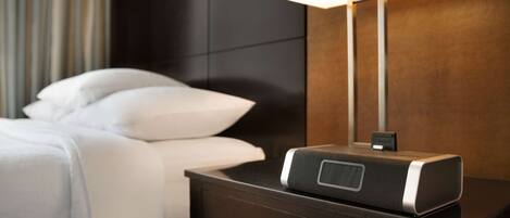 A neatly made bed with white linens, a bedside table with a lamp, and a small drawer.