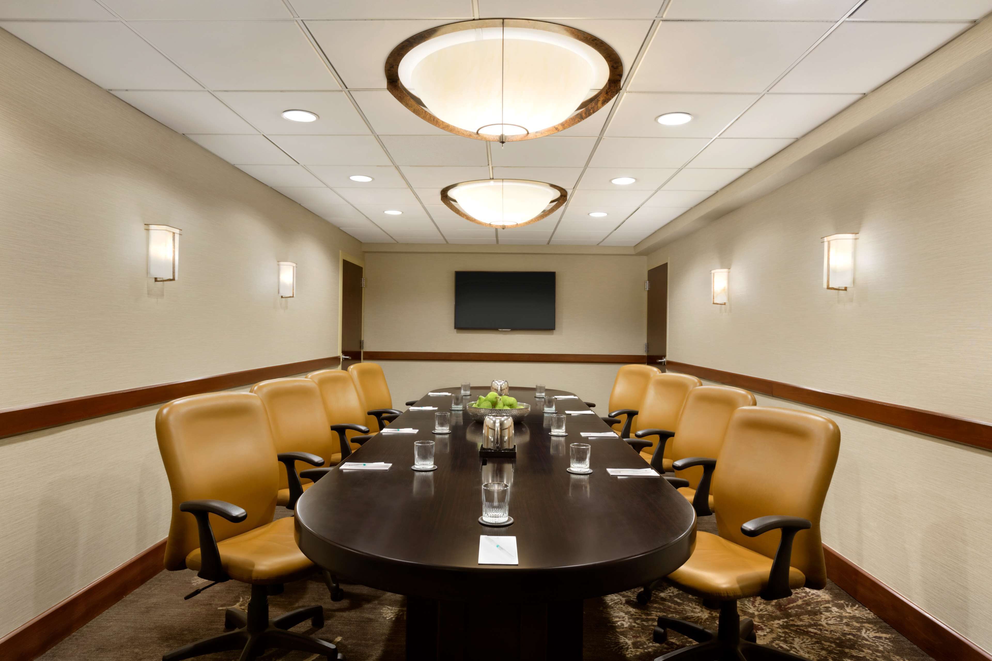 A conference room with a round table, 10 chairs, and a large screen on the wall.