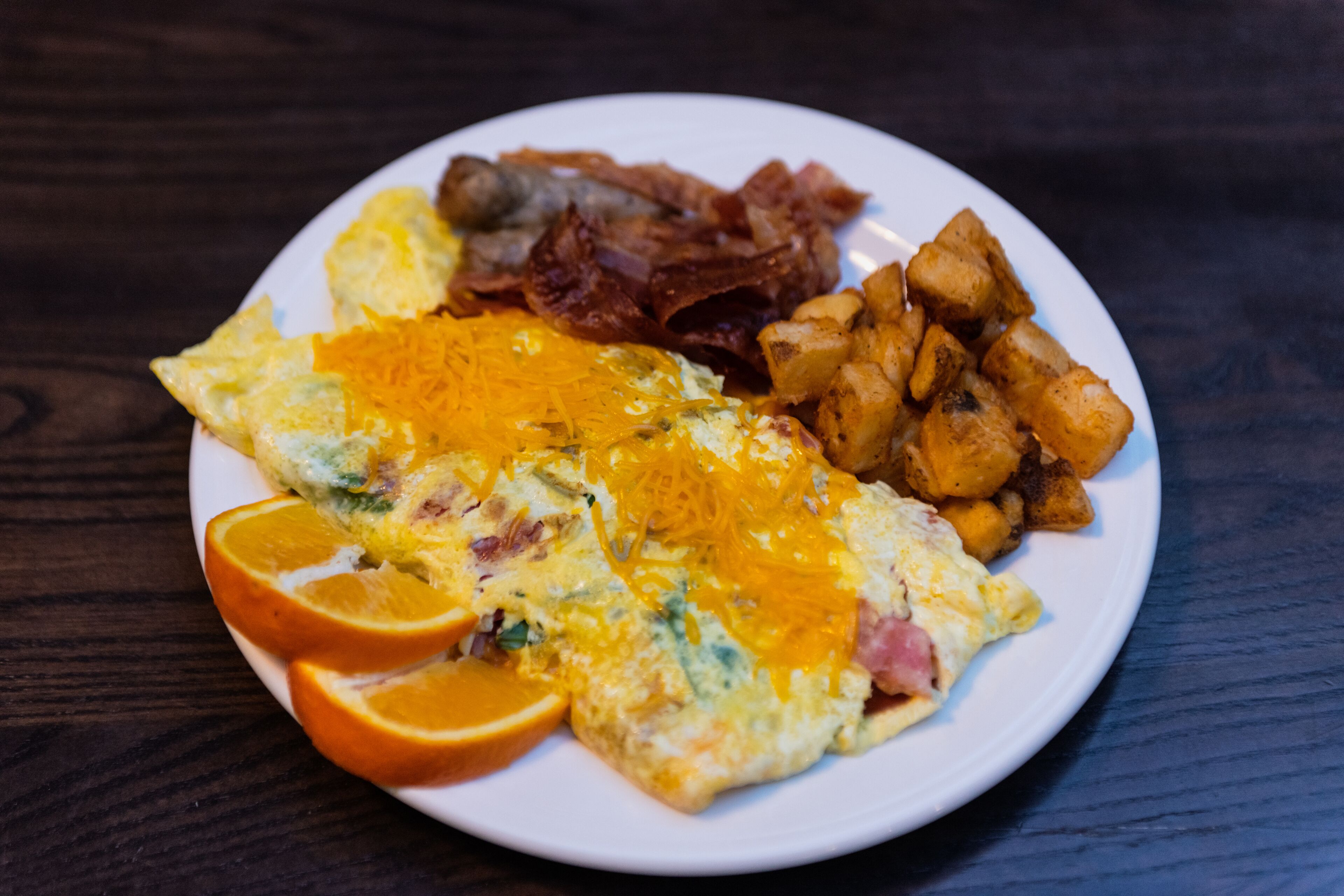 A plate with an omelette, bacon, and roasted potatoes.