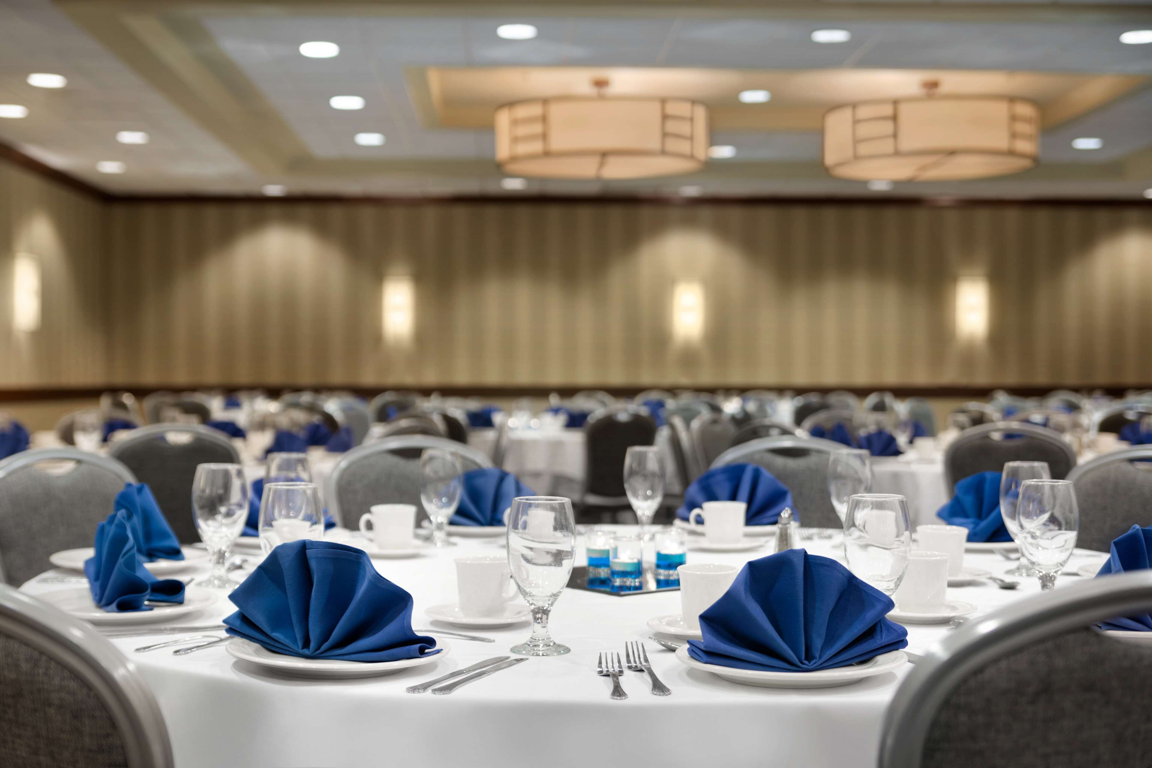 A banquet hall with round tables set for a formal event, featuring white tablecloths, blue napkins, and silverware.