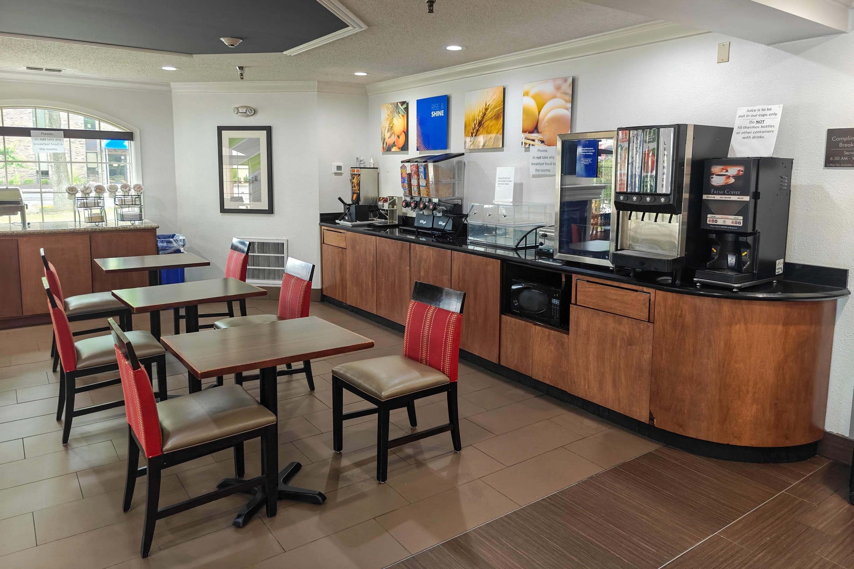 A breakfast area with tables, chairs, a coffee machine, and a juice dispenser.
