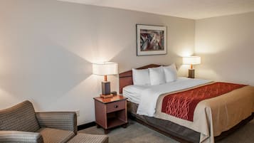 A hotel room with a bed, two bedside lamps, a small nightstand, a chair, and a painting on the wall.