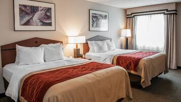 Ein Hotelzimmer mit zwei Betten, jeweils mit weißer Bettwäsche und einer roten Decke. Zwei Nachttischlampen, ein gerahmtes Bild an der Wand und ein Fenster mit Vorhängen sind ebenfalls vorhanden.