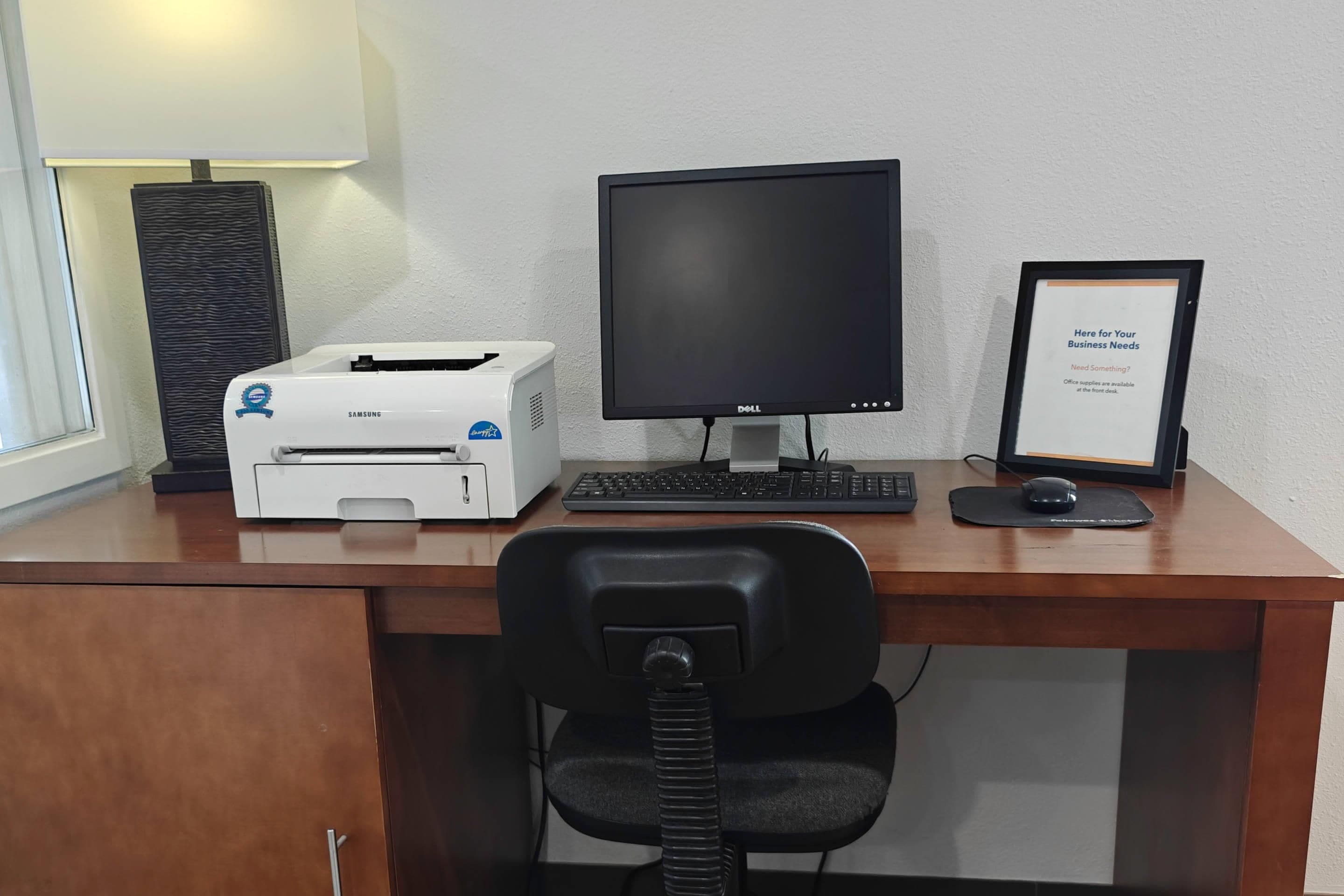 A desk with a computer, a printer, a framed sign, and a chair.