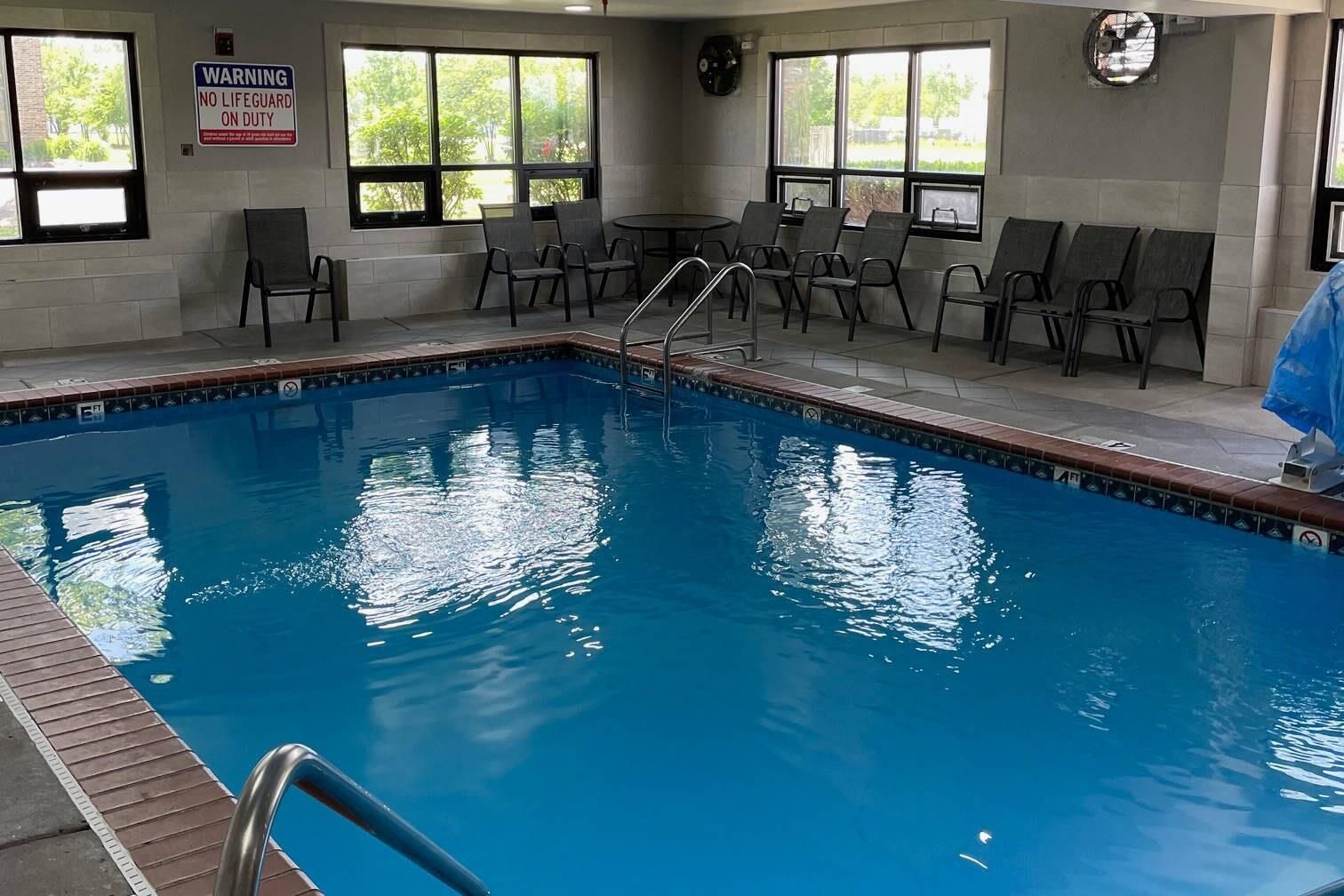 An indoor swimming pool with a lifeguard warning sign, chairs, and a clock on the wall.