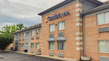 Un edificio de ladrillo con un letrero que dice 'Comfort Inn'. Hay varias ventanas, algunas con toldos, y un estacionamiento al frente.