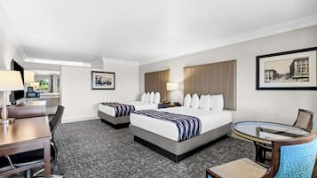 Quarto de hotel com duas camas, uma escrivaninha, uma cadeira, uma mesinha e um abajur.