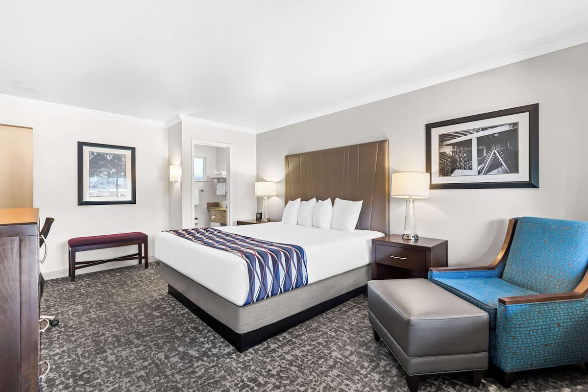 A hotel room with a large bed, a bench, a chair, a desk, and a framed picture on the wall.