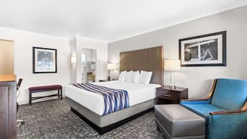 A hotel room with a large bed, a bench, a chair, a desk, and a framed picture on the wall.