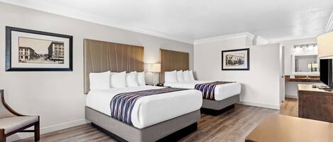 A hotel room with two beds, a desk, a chair, and a television.