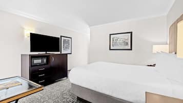 A hotel room with a bed, a TV on a stand, a desk with a chair, and two framed pictures on the wall.