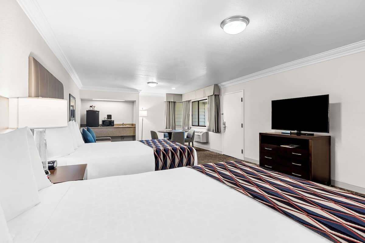 A hotel room with two beds, a TV, a desk, and a bathroom.