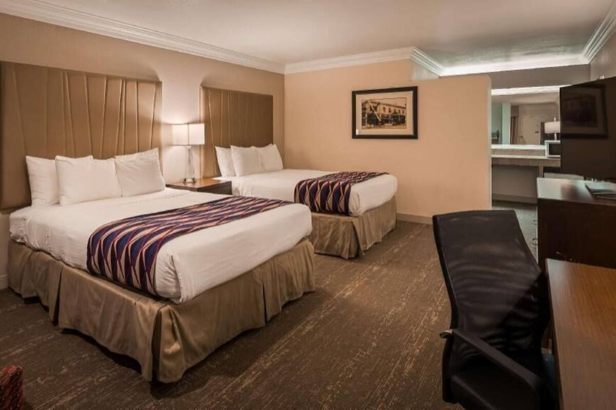 A hotel room with two beds, a desk, a chair, a TV, and a bathroom visible in the background.