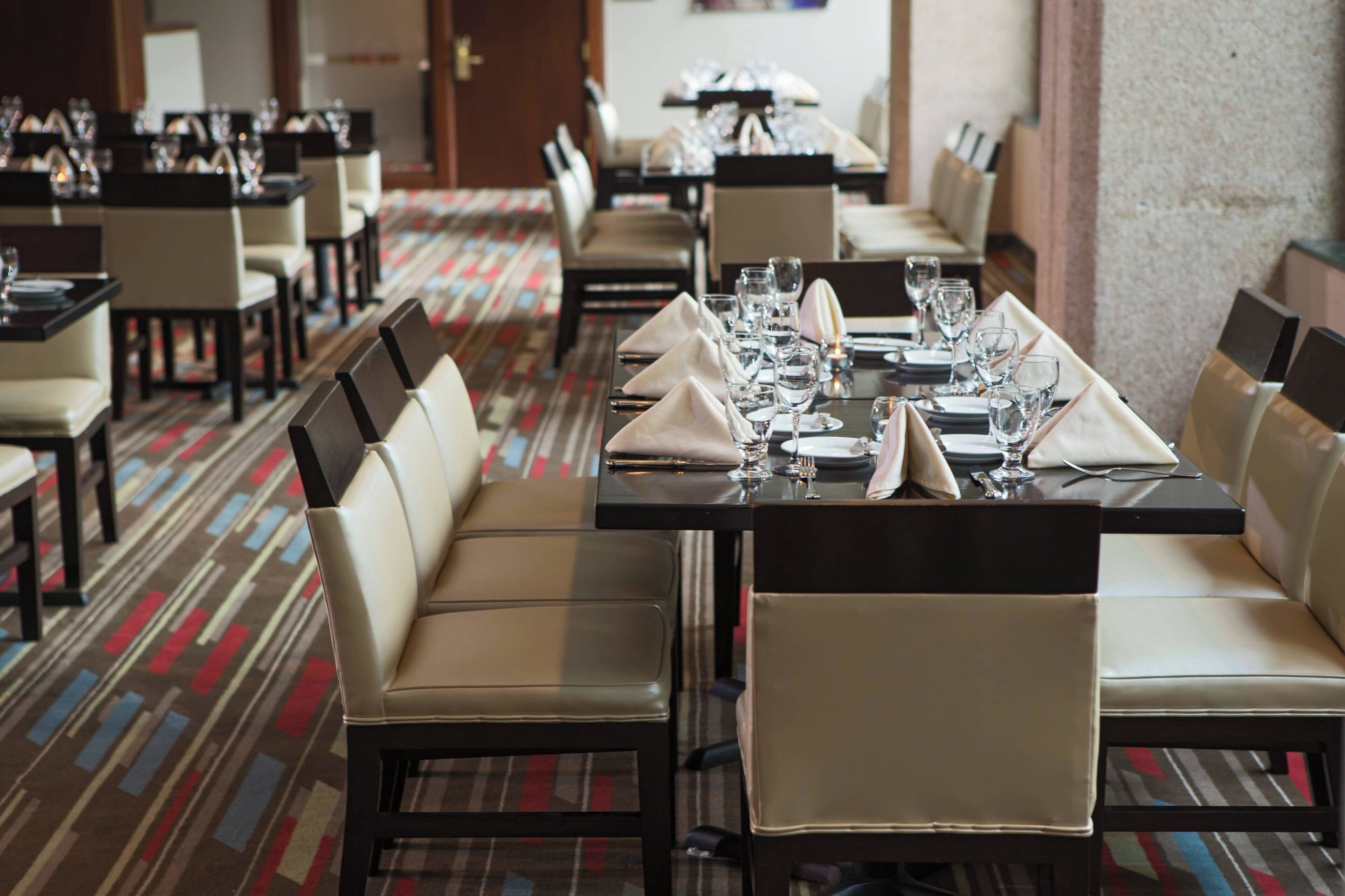 A hotel dining area with multiple tables set for service, each with chairs and table settings.
