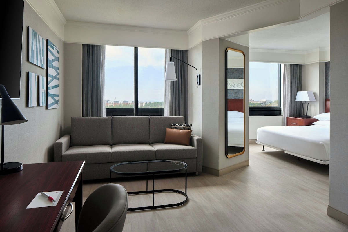 Habitación de hotel con sofá, cama, escritorio y un amplio ventanal con vistas a la ciudad.