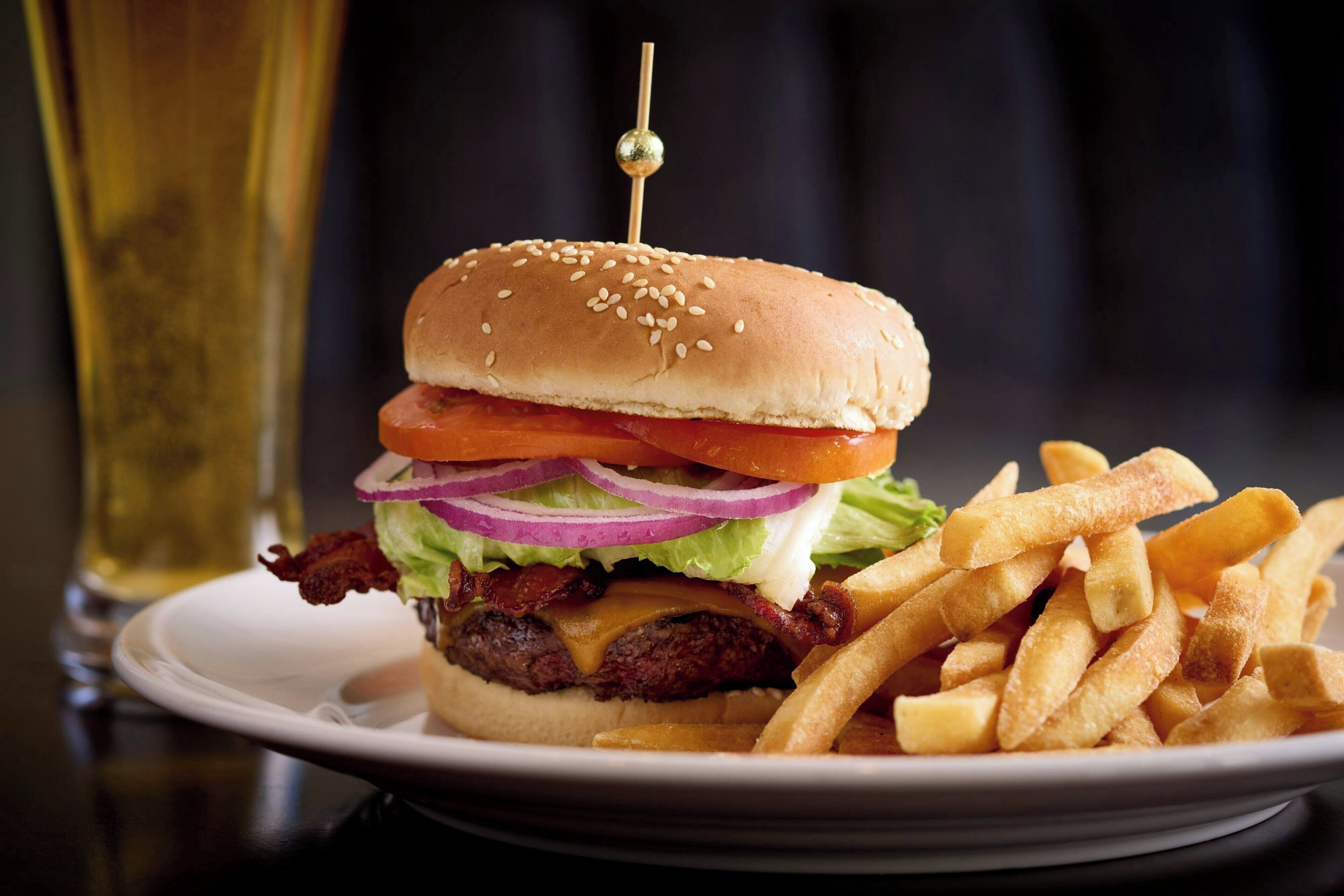 Hamburguesa con lechuga, tomate, cebolla y pan con semillas de sésamo, acompañada de papas fritas en un plato.