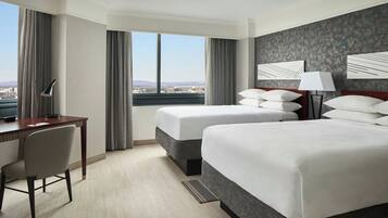 A hotel room with two beds, a desk, and a view of the city.