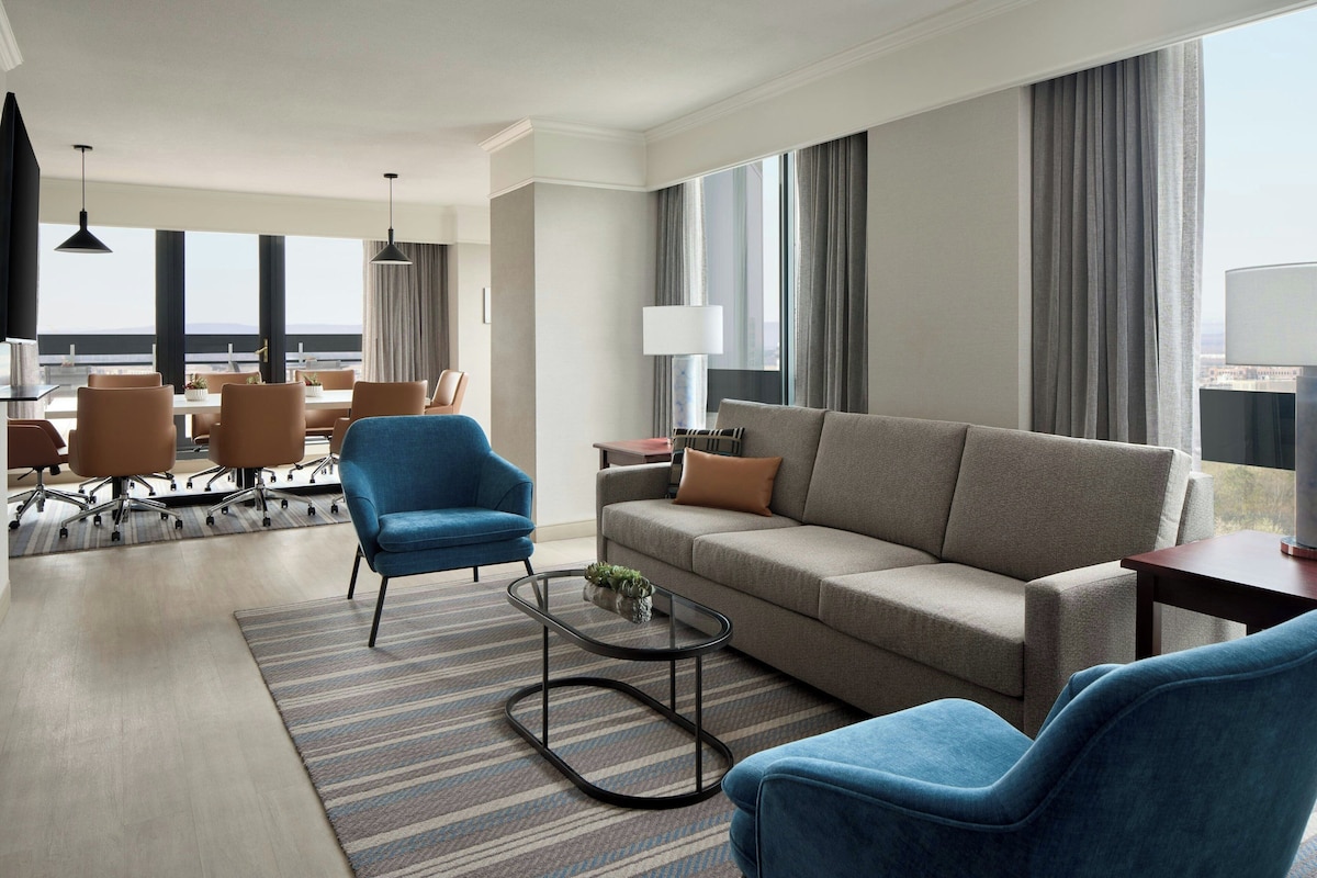 Una habitación de hotel moderna con sofá, dos sillones, una mesa de centro y un área de comedor con sillas y una mesa.