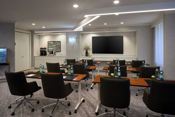 A conference room with tables, chairs, a large flat-screen TV, and a coffee station.
