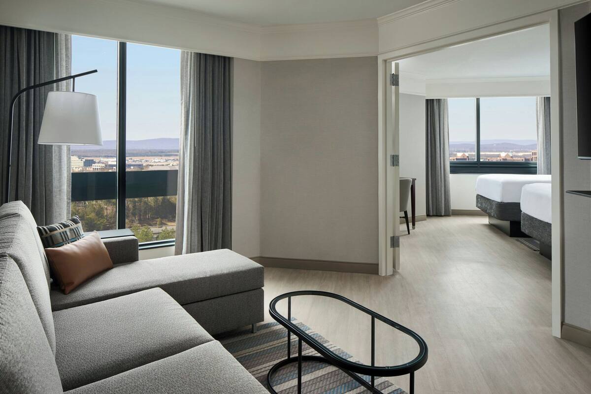 A modern hotel room with a large window, a sofa, a small table, and a bed.