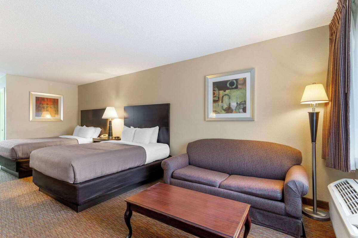 A hotel room with two beds, a sofa, a coffee table, a lamp, and artwork on the walls.