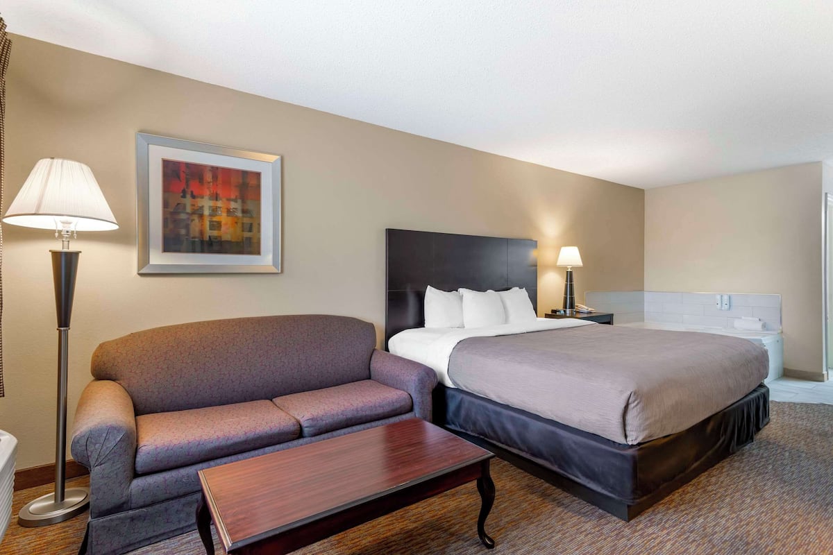 A hotel room with a bed, a sofa, a small table, and a painting on the wall.