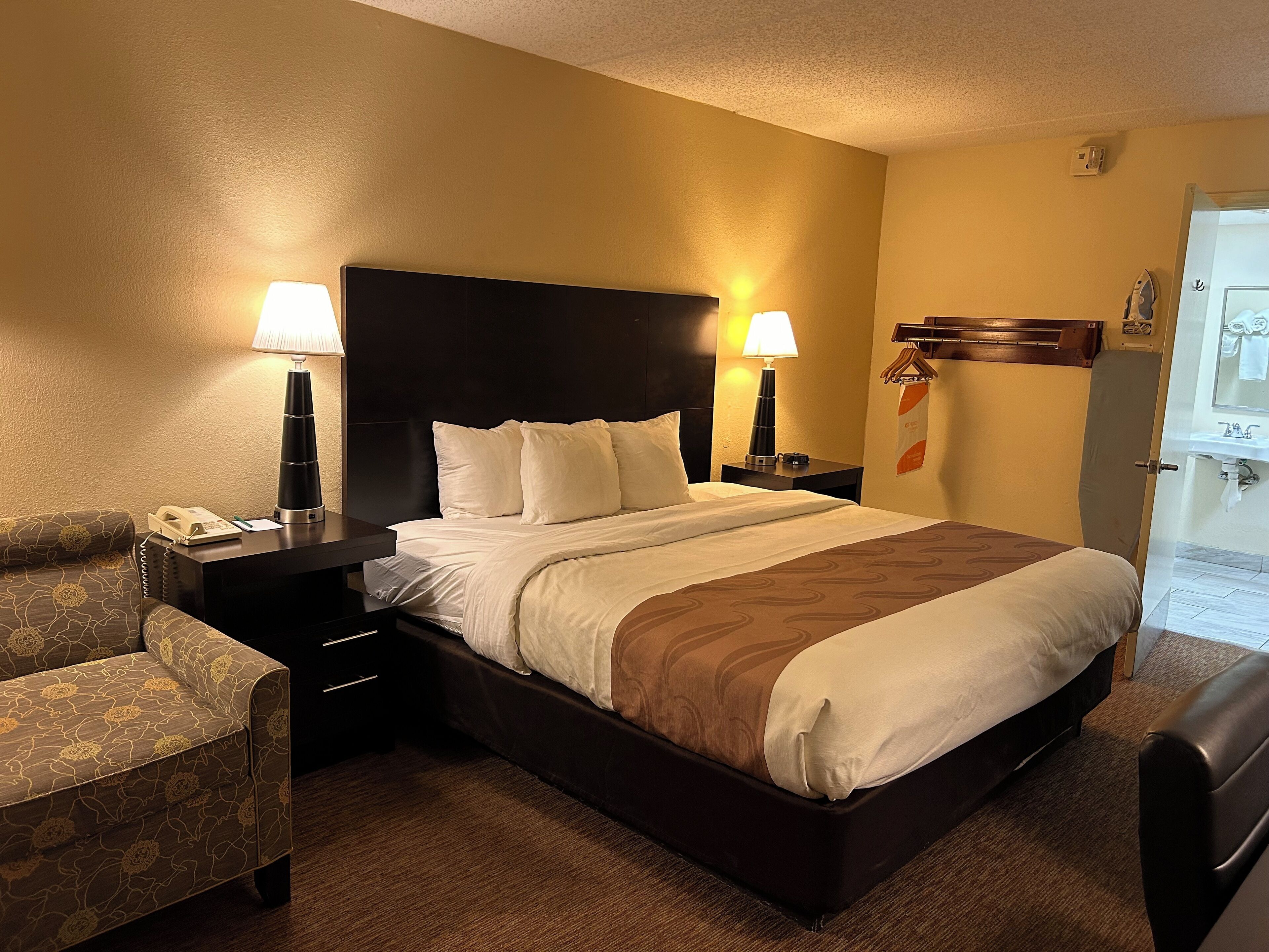 Une chambre d’hôtel avec un grand lit, deux tables de chevet avec des lampes, une chaise et une porte donnant sur une salle de bain.