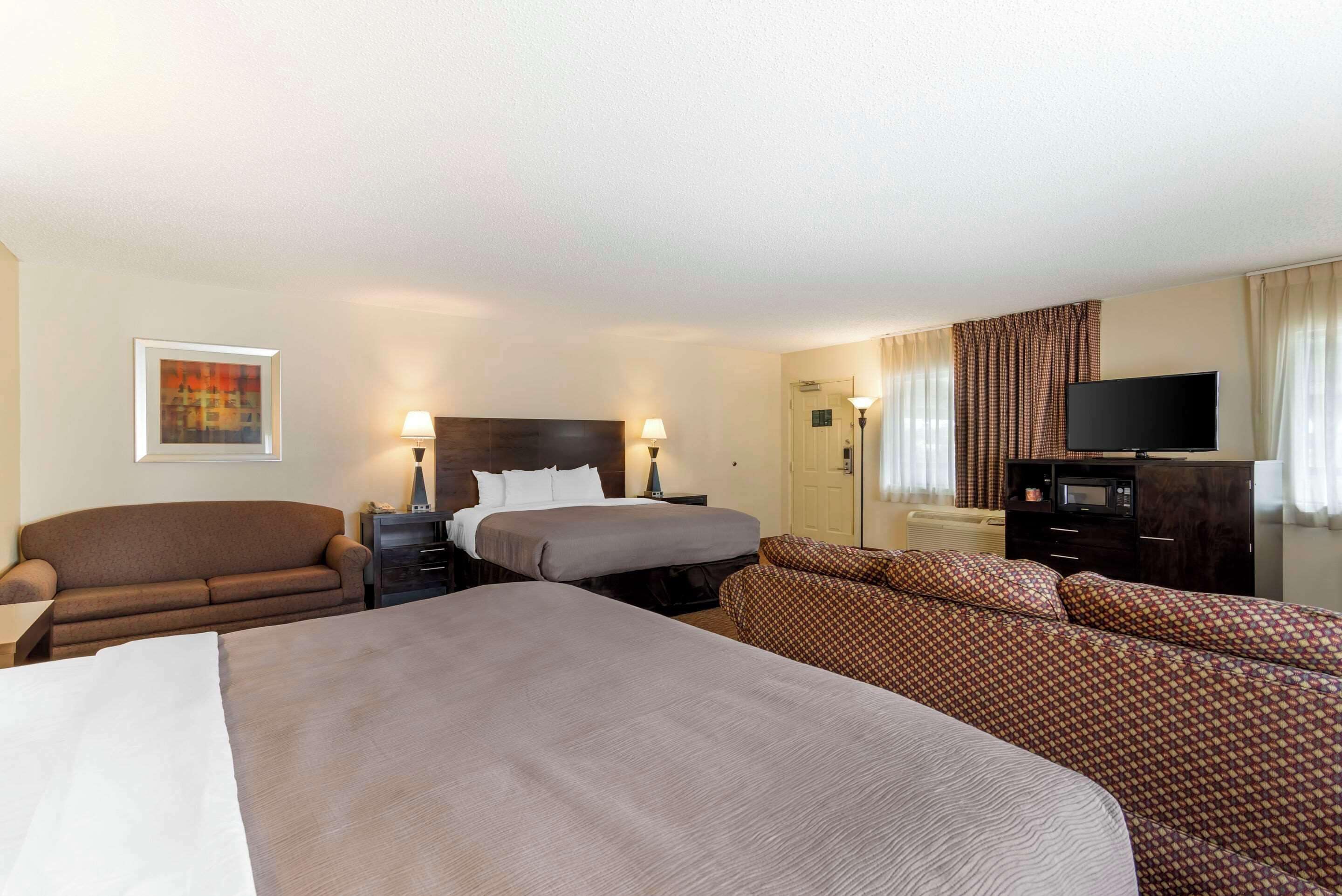 Habitación de hotel con una cama grande, un sofá, un televisor y un escritorio con lámpara.