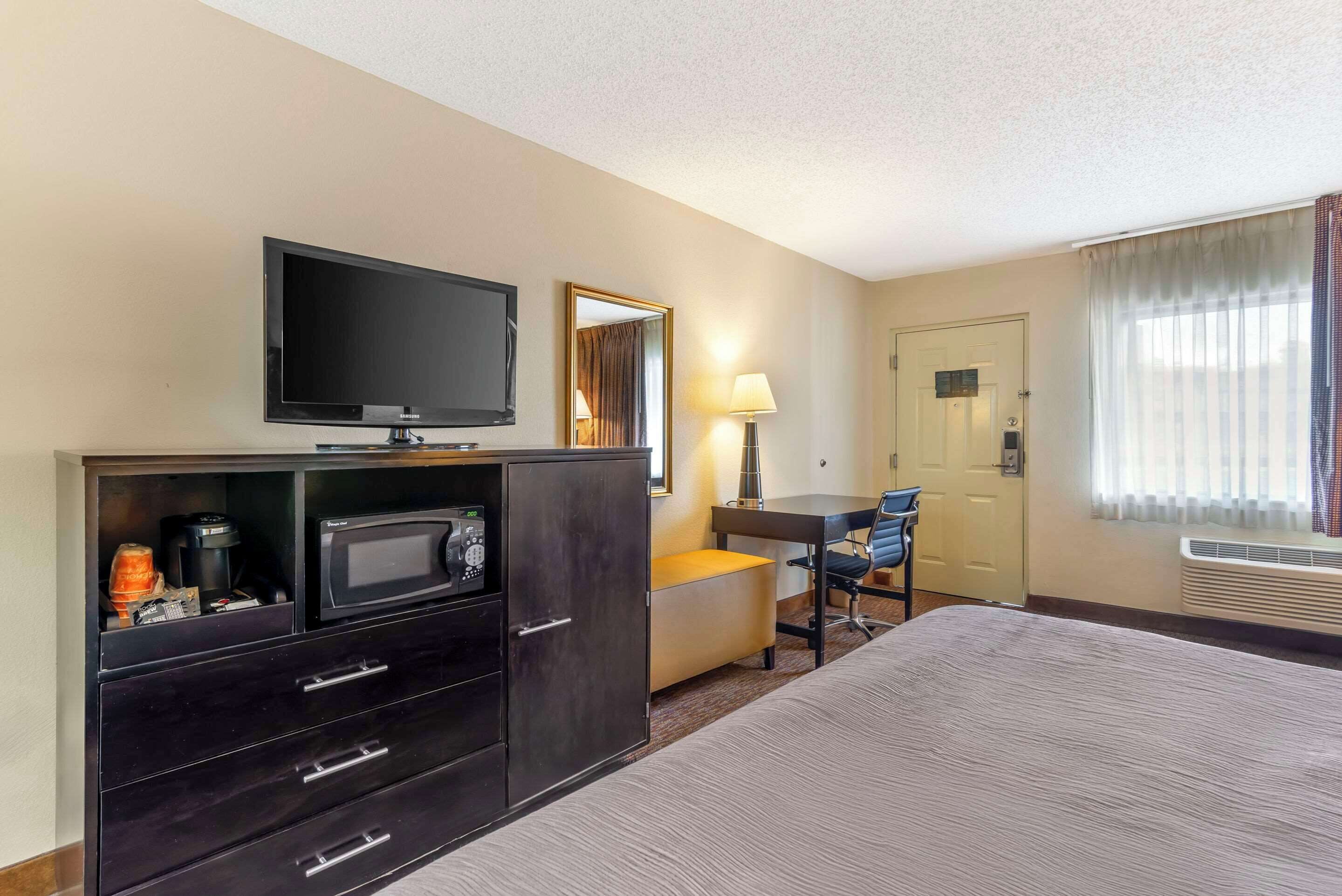 A hotel room with a bed, a TV, a desk with a chair, a lamp, and a microwave.