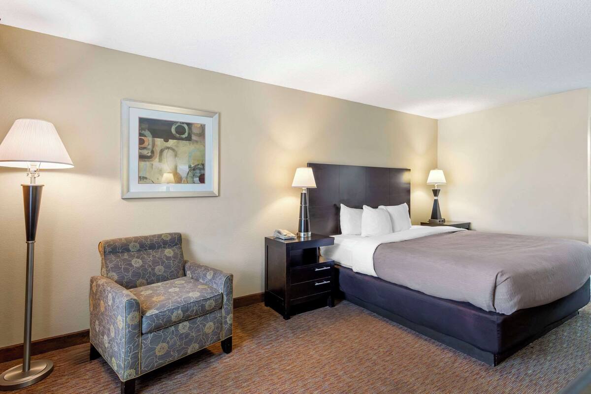 A hotel room with a bed, a chair, two bedside tables, and a floor lamp.