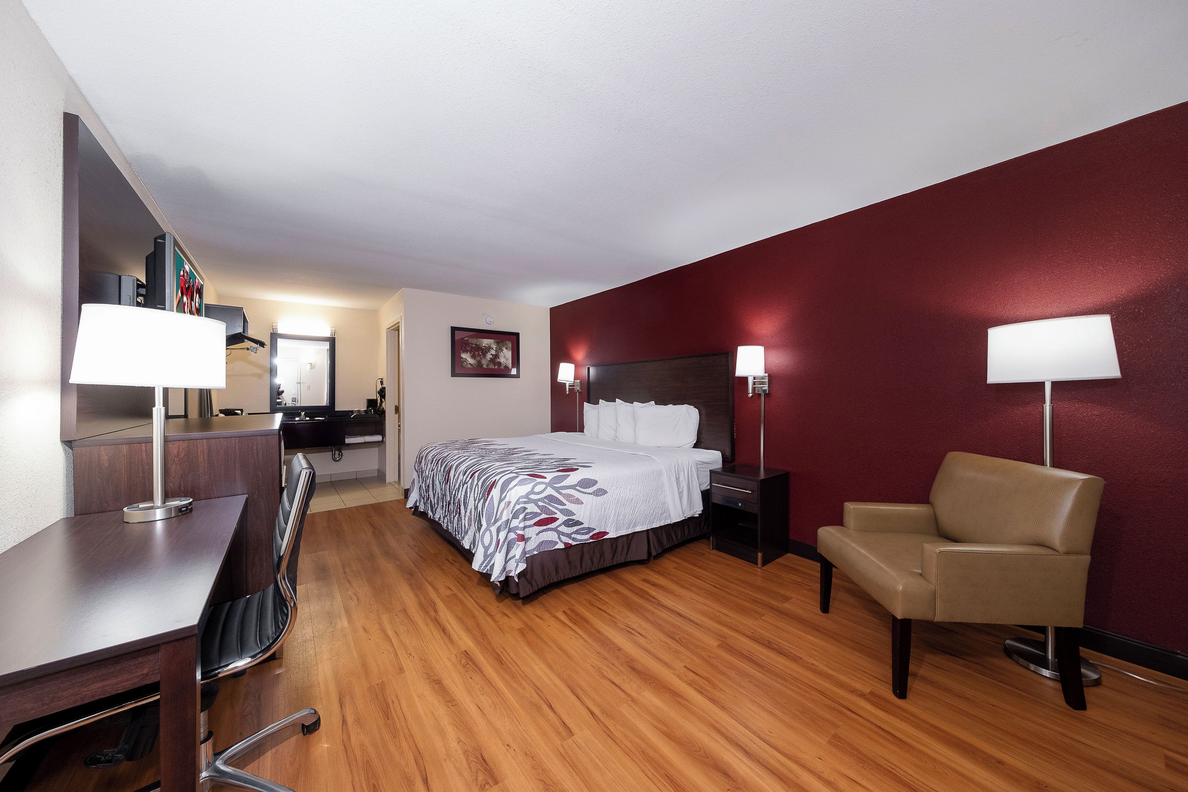Una habitación de hotel con una cama, lámparas de noche, un escritorio, una silla y un espejo.