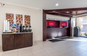 A hotel reception area with a coffee station, a red sign indicating free Wi-Fi in all rooms, and a view of the outside balcony. - Red Roof Inn Bordentown - McGuire AFB (Bordentown)