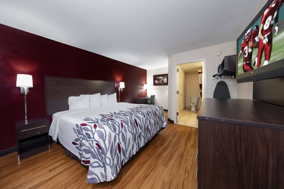 A hotel room with a large bed, a desk, a TV, and a bathroom visible through an open door.