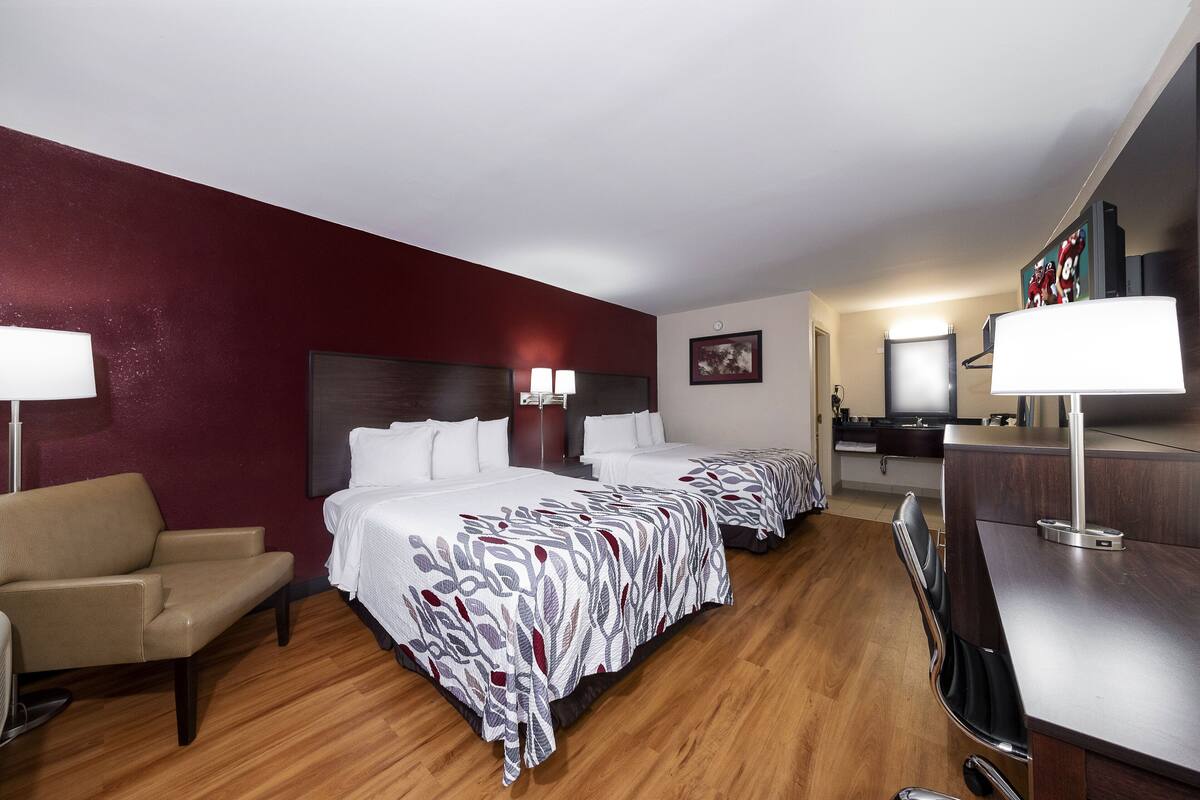 Habitación de hotel con dos camas, un escritorio, una silla y un televisor.
