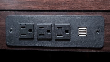 A black electrical outlet with three standard sockets and a USB port on a wooden surface.