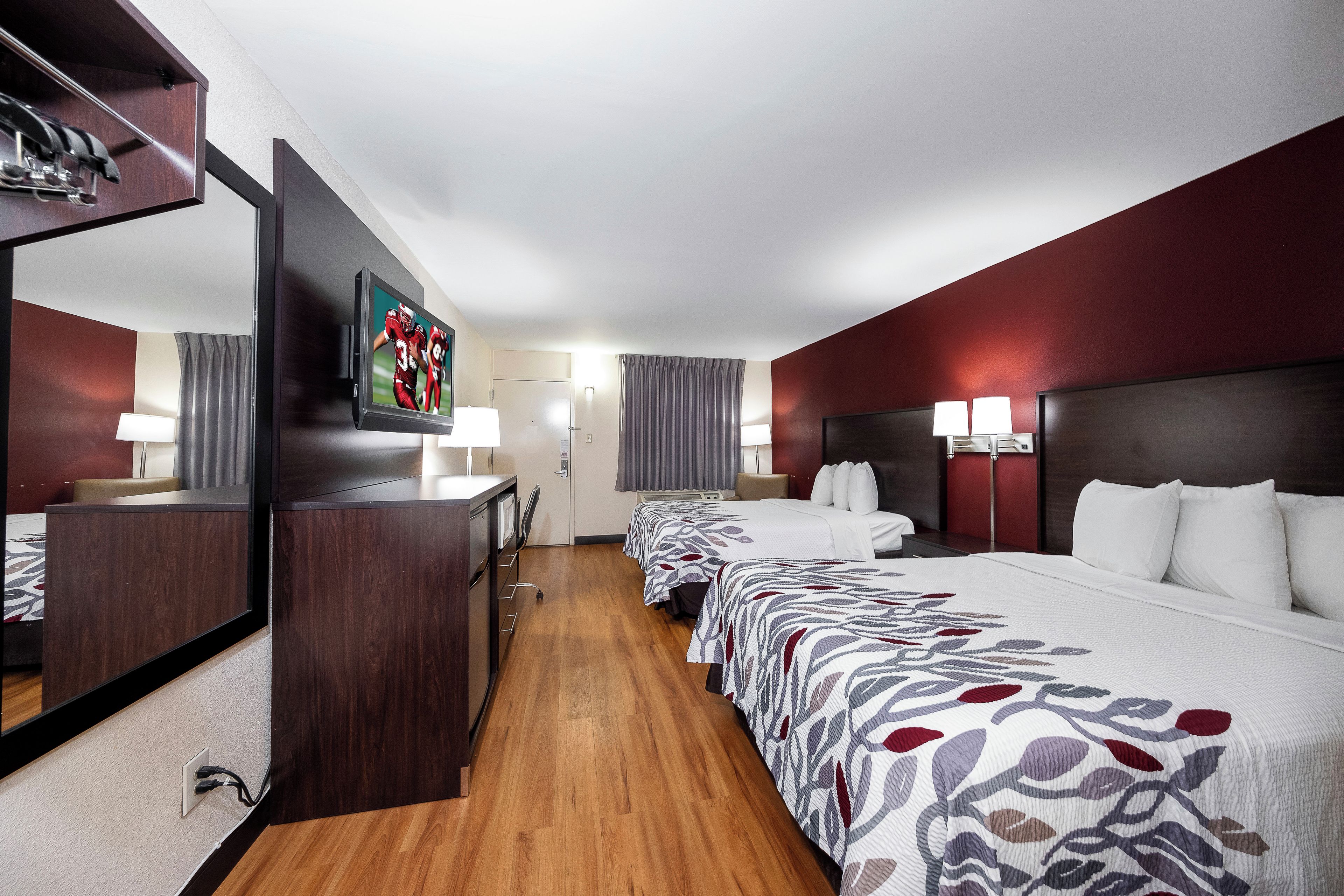 A hotel room with a large bed, a desk, a television, and a mirror.