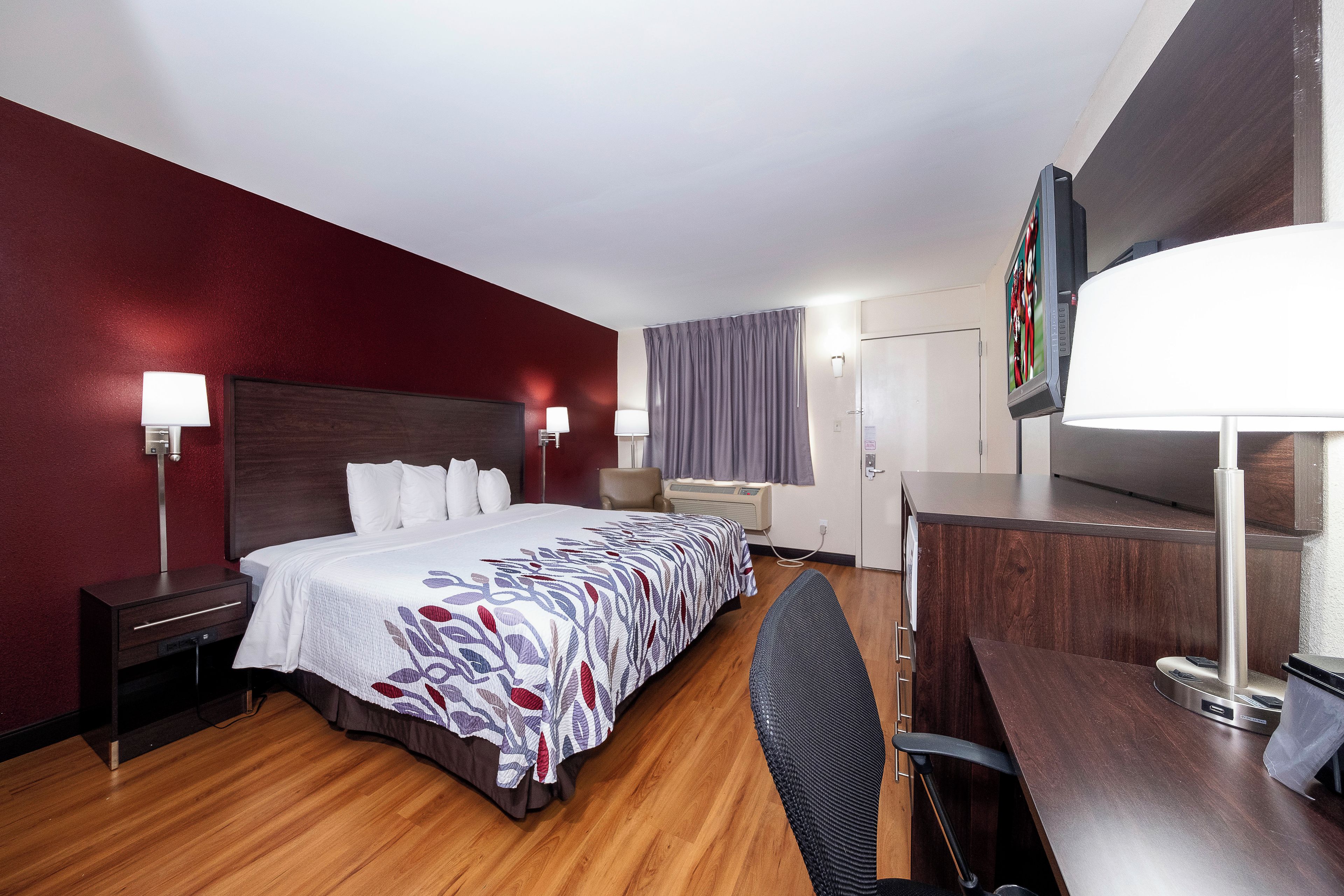 Une chambre d’hôtel avec un grand lit, des lampes de chevet, un bureau avec une chaise, une télévision et une fenêtre avec des rideaux.