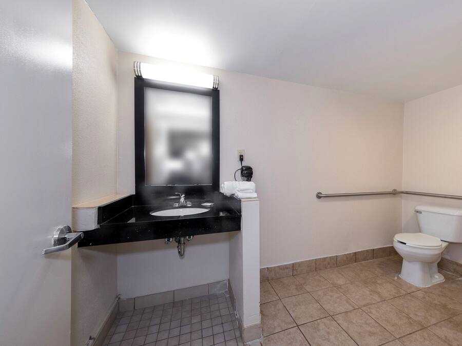 A bathroom with a black sink, a mirror, a toilet, and a handrail.