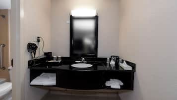 A compact bathroom with a black vanity, a white sink, and a mirror above. There is a towel rack and a hand dryer on the wall.