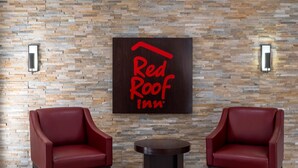 A Red Roof Inn sign on a stone wall, two red leather chairs, and a small round table. - Red Roof Inn Bordentown - McGuire AFB (Bordentown)