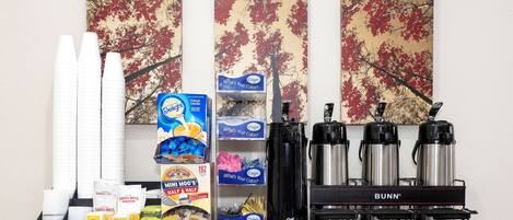 A kitchen counter with various items including paper cups, creamer, coffee makers, and a coffee machine.