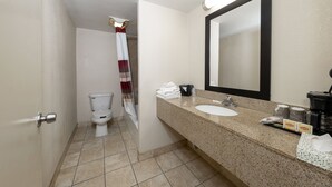 Un baño con inodoro, lavamanos y espejo. Hay toallas y artículos de aseo en la encimera.