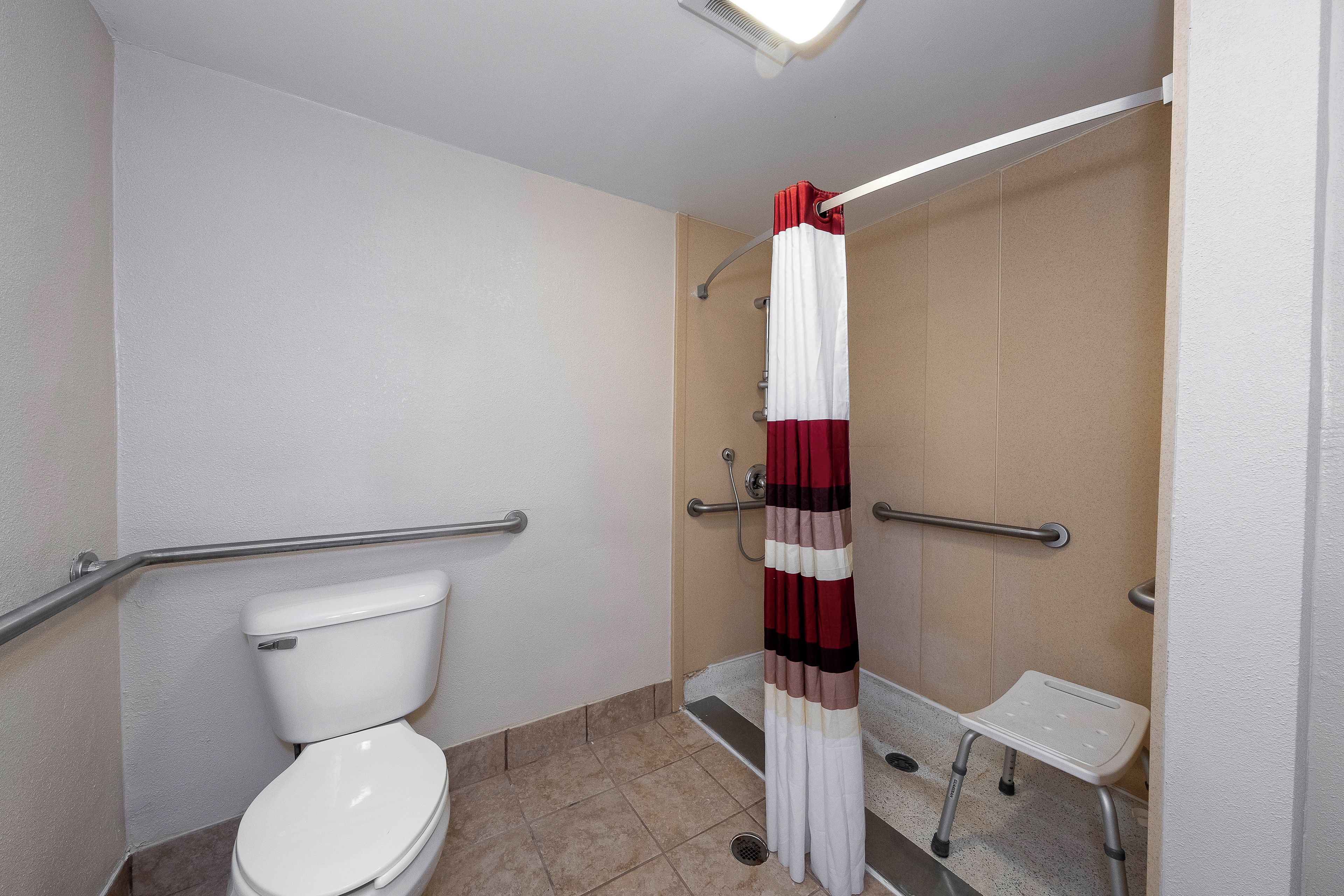 Ein Badezimmer mit einer weißen Toilette, einer Dusche mit einem roten und weißen Streifenrollo und einer Haltestange.