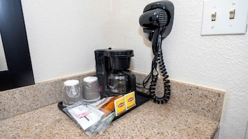 Cocina de una habitación de hotel con una cafetera, un teléfono y una bandeja con bolsitas de té Lipton.