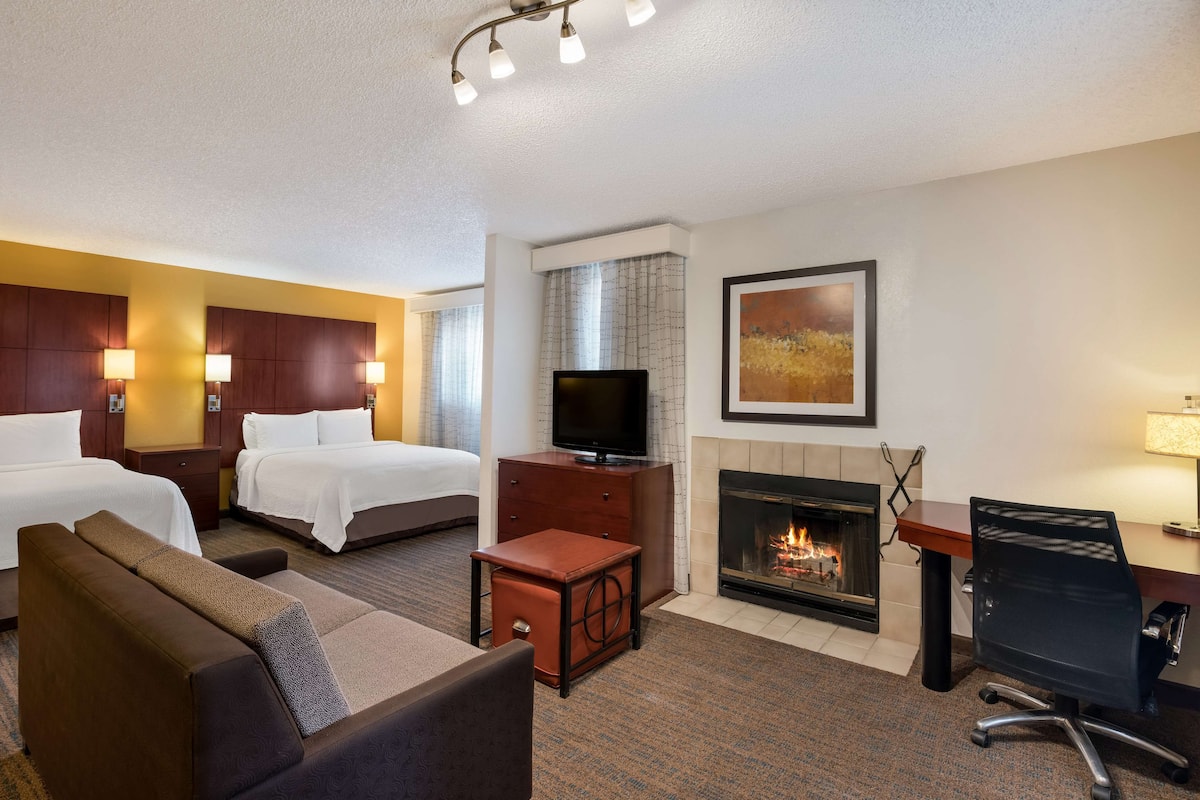 A hotel room with two beds, a TV, a fireplace, a desk, and a couch.