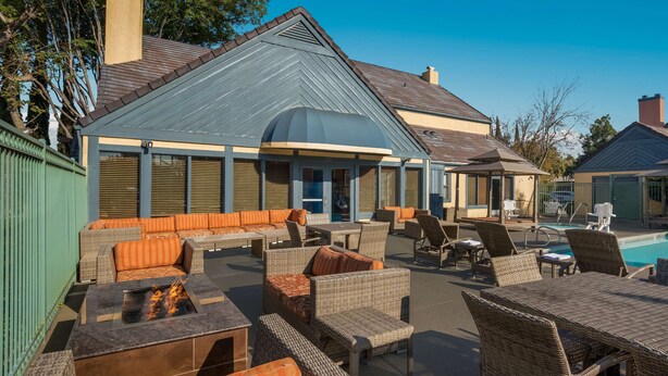 An outdoor lounge area with wicker furniture, a fire pit, and a pool. - SenS Suites Livermore, SureStay Collection by Best Western (Livermore)