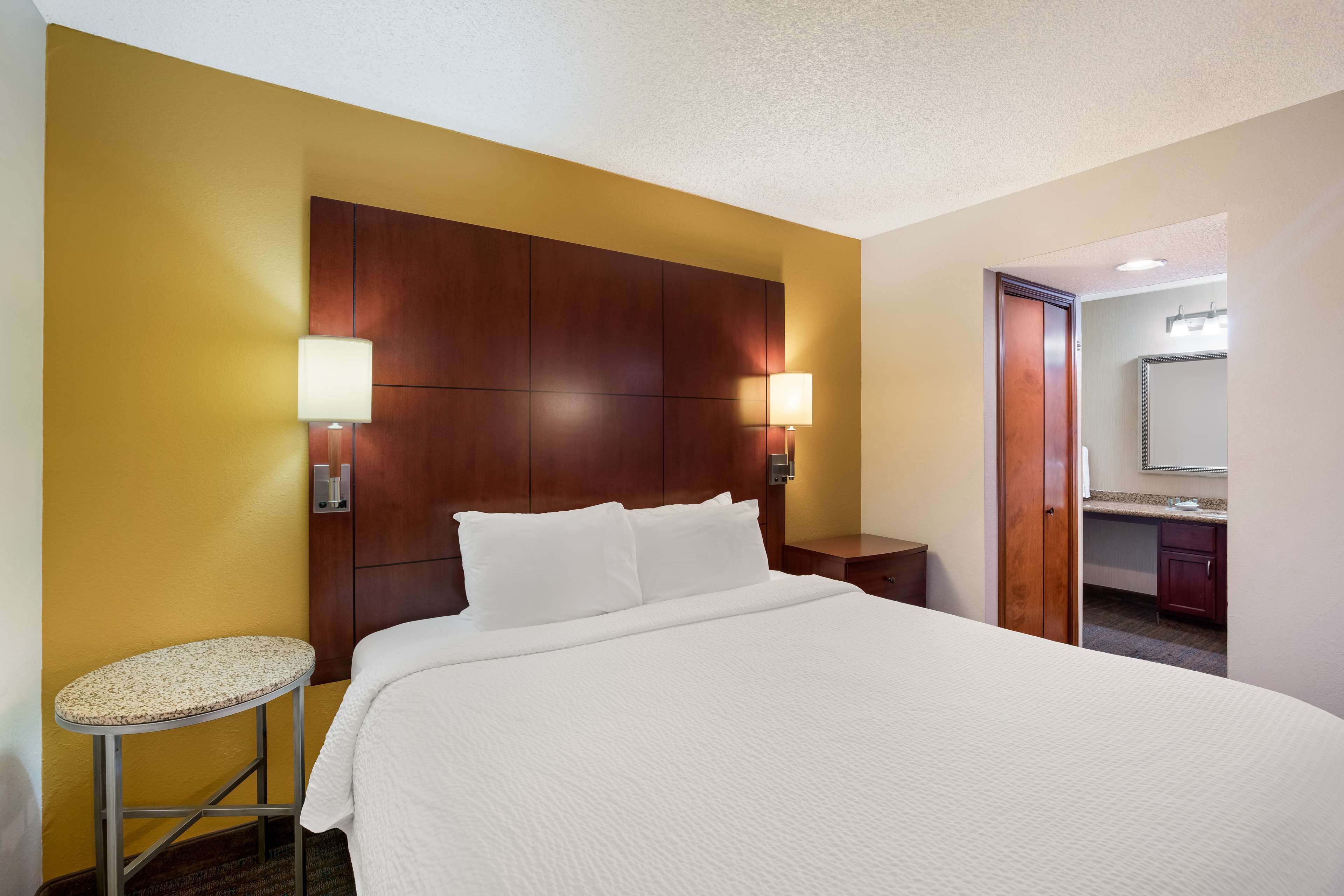 A hotel room with a large bed, two bedside lamps, a small round table, and a mirror.
