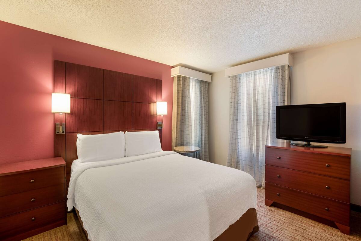 A hotel room with a large bed, a wooden dresser, a television, and a small table.