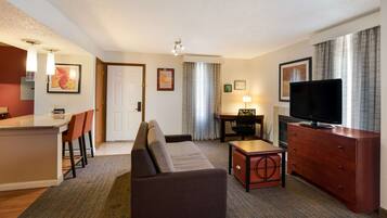 A hotel room with a living area, a dining area, a sofa, a TV, and a desk.